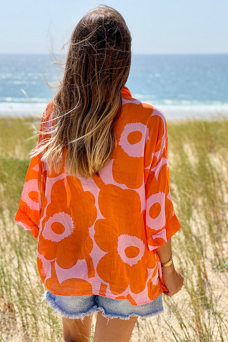 Blusa ligera de voile de algodón rosa con estampado de grandes flores naranjas y cuello camisero en pico.