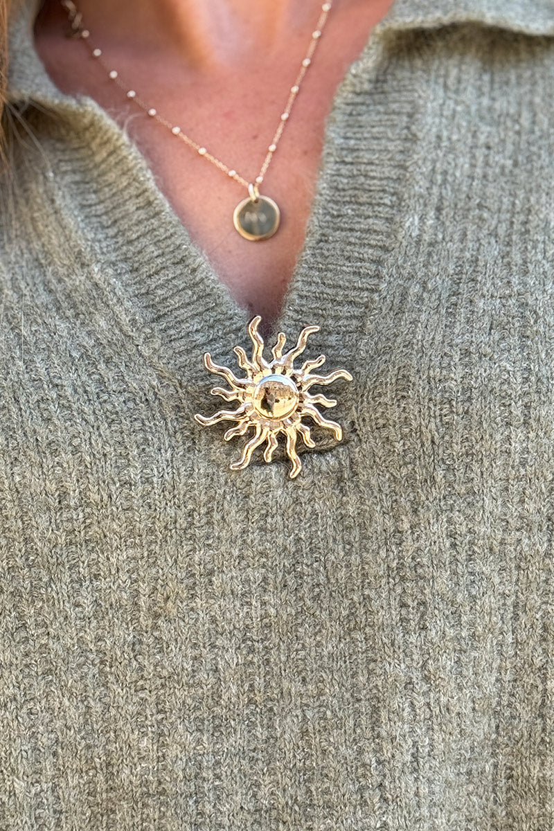 Suéter de punto color caqui jaspeado con mangas 3/4, cuello de camisa y broche dorado de sol.